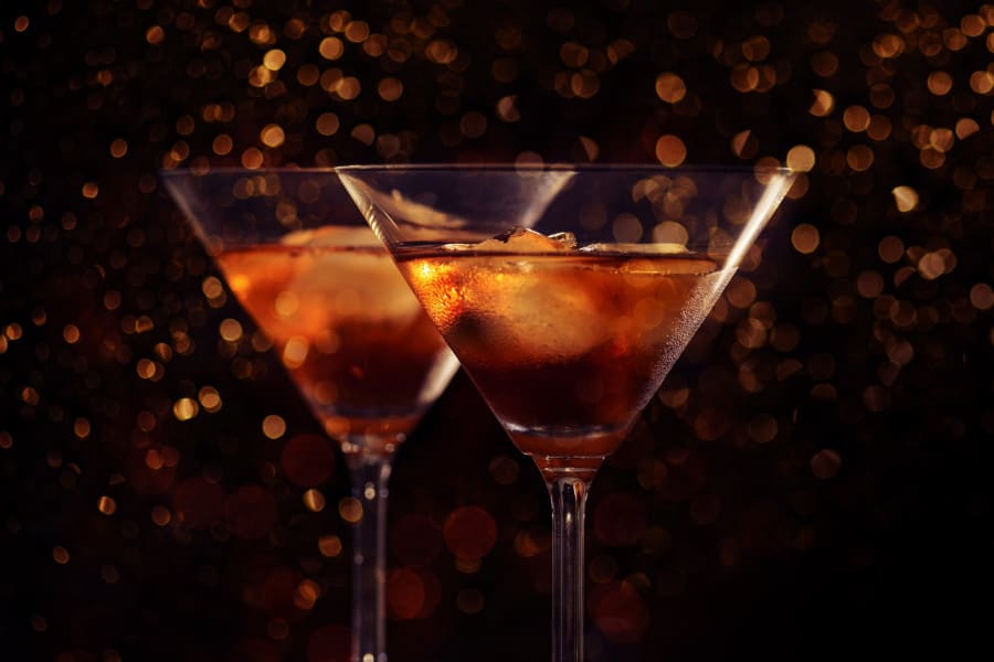 Two martini glasses filled with amber-colored drinks and ice, set against a dark background with warm golden bokeh lights, creating a festive and elegant atmosphere.